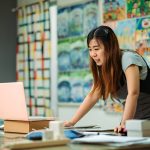 woman using a laptop, with artworks behind her