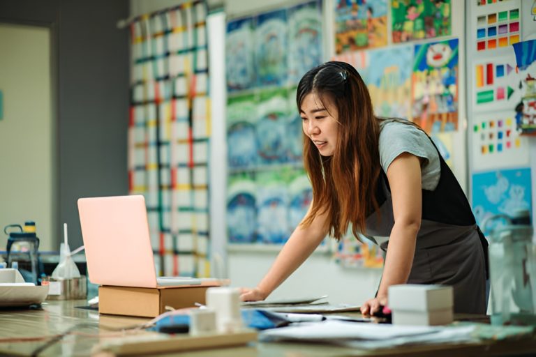 woman using a laptop, with artworks behind her