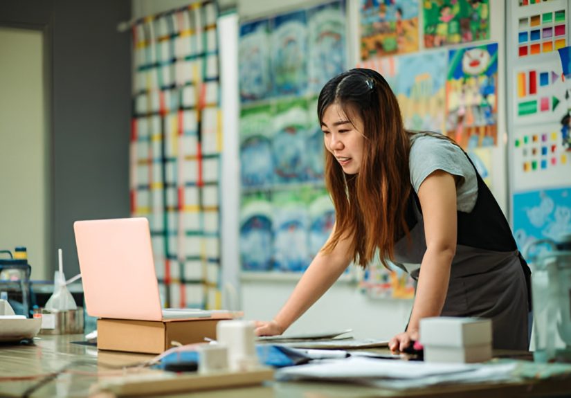 woman using a laptop, with artworks behind her