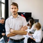 man standing in a conference room, with his colleagues sitting behind him